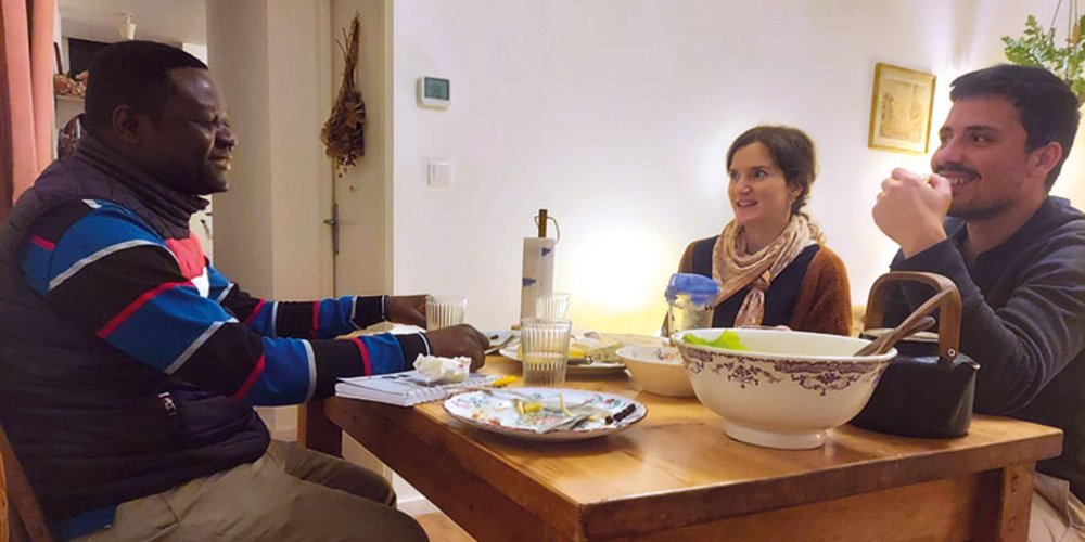 Un homme est assis à table face à un couple, qui l’écoutent, devant des assiettes vides et un saladier.
