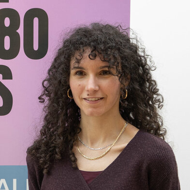 Jeune femme aux cheveux bruns et bouclés, devant un kakémono violet