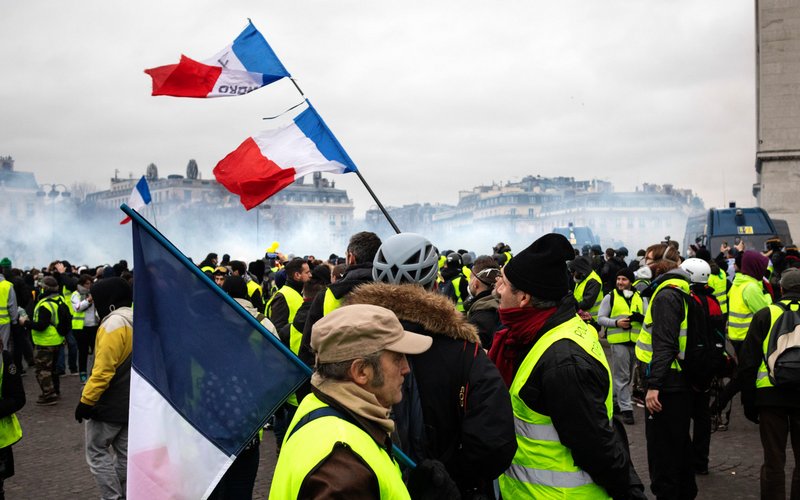 Personnes avec gilets jaunes au 1er plan, drapeau français dressé et fumigènes en fond