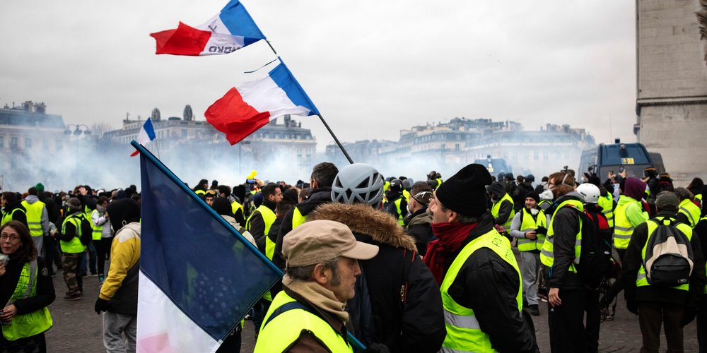 Personnes avec gilets jaunes au 1er plan, drapeau français dressé et fumigènes en fond