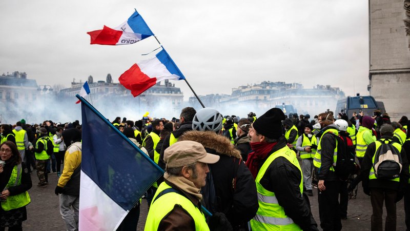 Personnes avec gilets jaunes au 1er plan, drapeau français dressé et fumigènes en fond