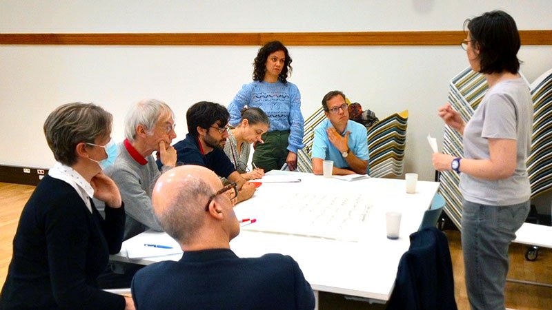 Huit personnes discutent autour d’une table (deux sont debouts)