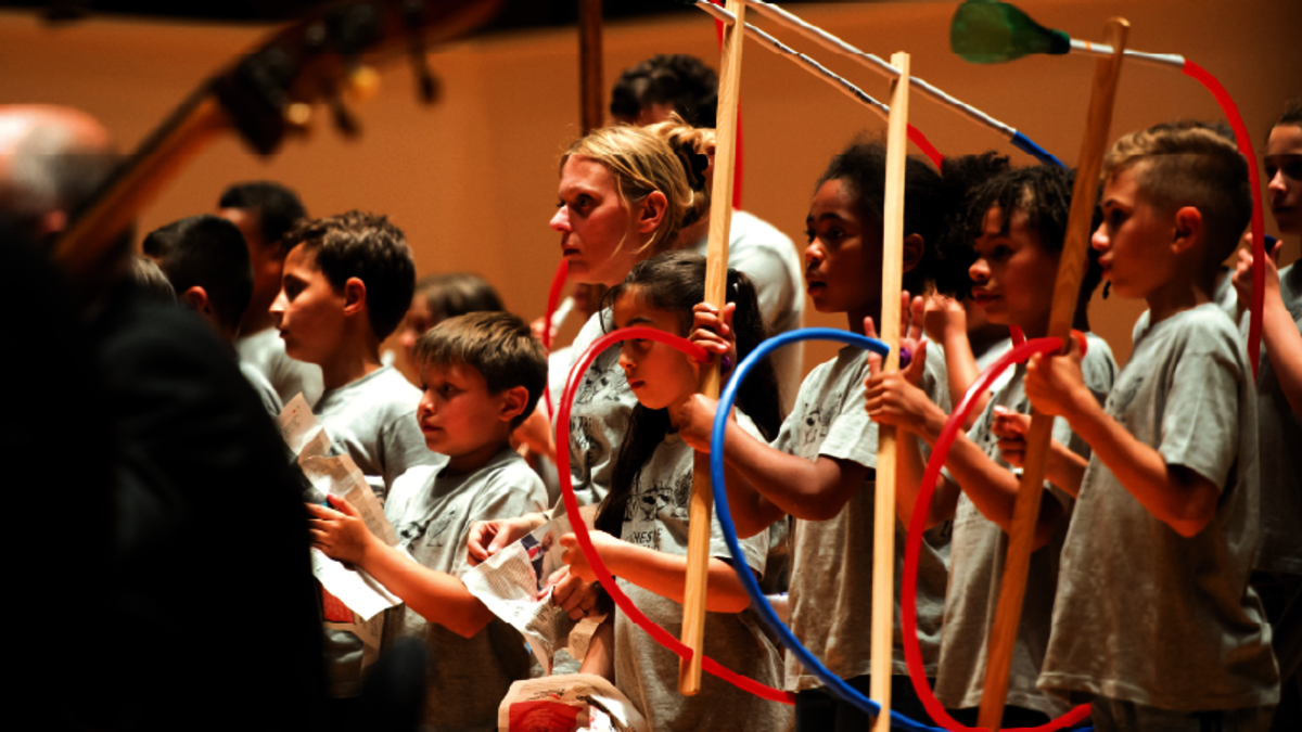 Enfants munis d’instruments en plasiques, derrière des musiciens