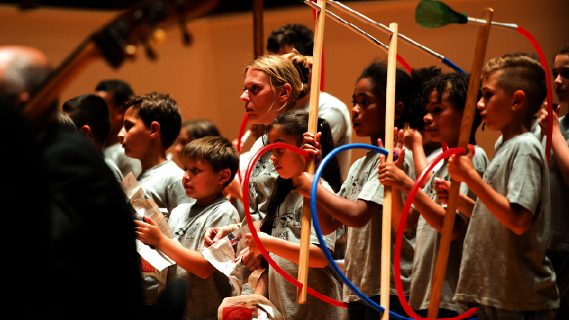 Enfants munis d’instruments en plasiques, derrière des musiciens
