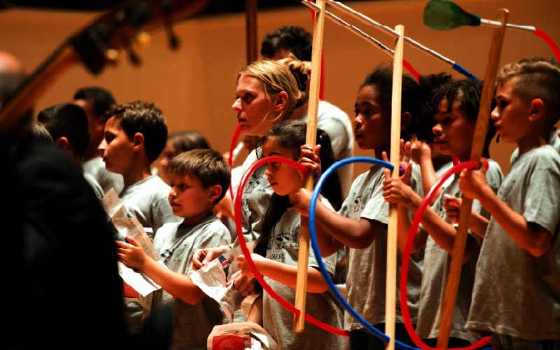 Enfants munis d’instruments en plasiques, derrière des musiciens