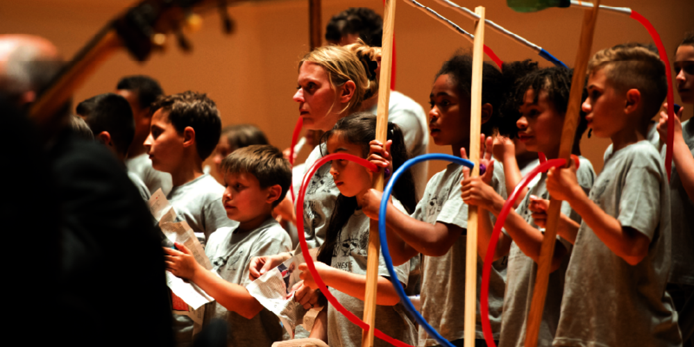 Enfants munis d’instruments en plasiques, derrière des musiciens