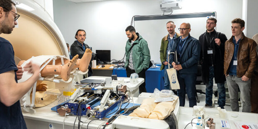Un groupe d’hommes en écoutent un autre, devant un mannequin, un IRM et divers appareils.