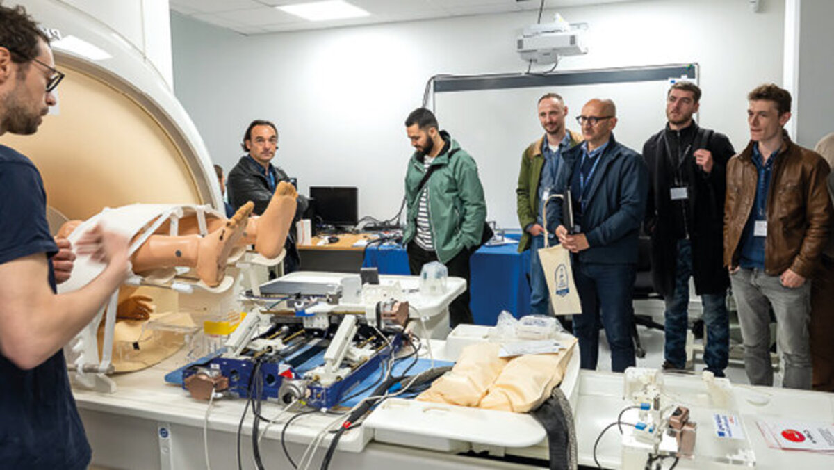 Un groupe d’hommes en écoutent un autre, devant un mannequin, un IRM et divers appareils.
