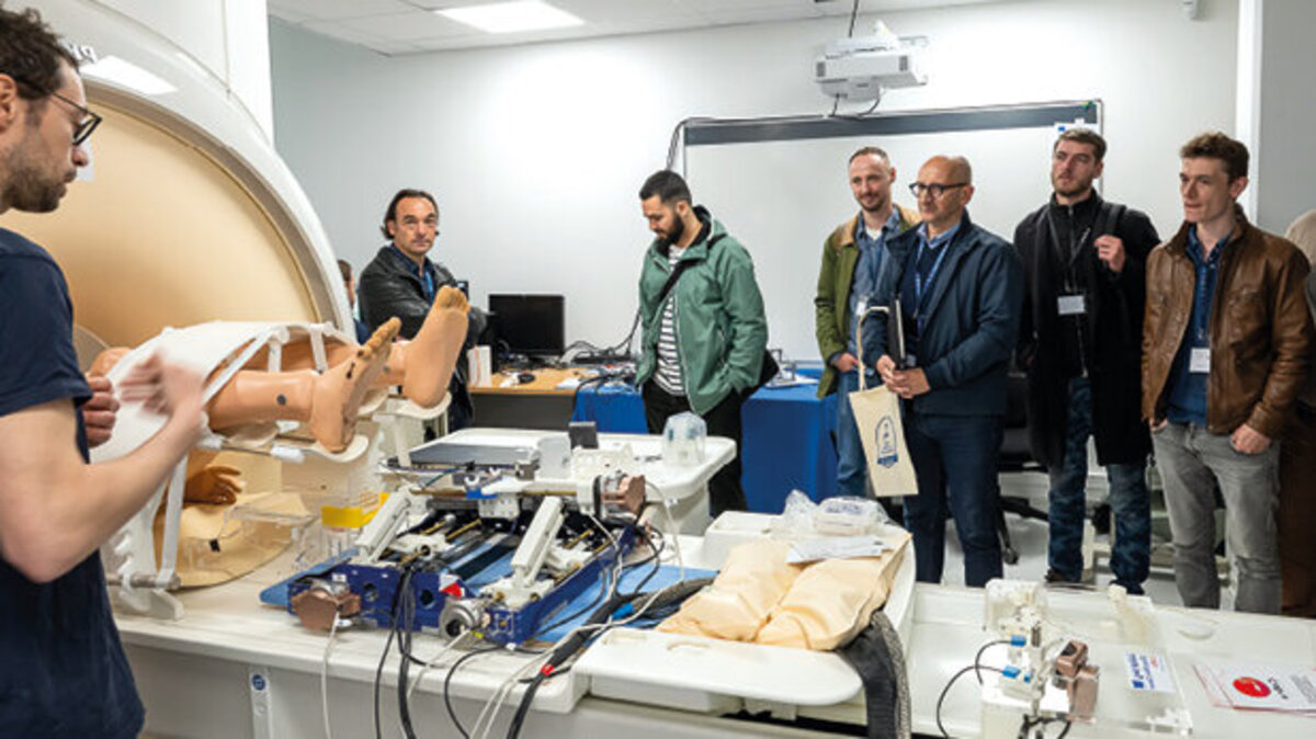 Un groupe d’hommes en écoutent un autre, devant un mannequin, un IRM et divers appareils.