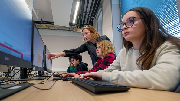 Deux jeunes filles de profil, face à des écrans. Une animatrice pointe quelque chose sur l’un d’eux.