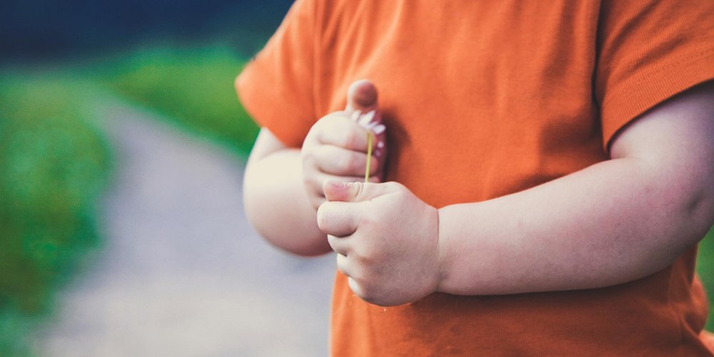 Image d’illustration montrant un enfant cadré au niveau des bras, sur un chemin, avec un t-shirt orange et tenant une fleur