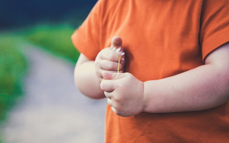 Image d’illustration montrant un enfant cadré au niveau des bras, sur un chemin, avec un t-shirt orange et tenant une fleur