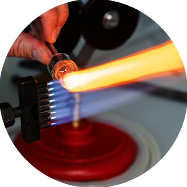 Un chalumeau constitué d’environ 8 flammes bleues parallèles, est appliqué sur un tube en verre, créant une trainée jaune.