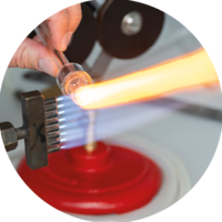 Un chalumeau constitué d’environ 8 flammes bleues parallèles, est appliqué sur un tube en verre, créant une trainée jaune.