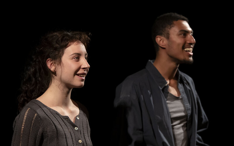 Une jeune femme et un jeune homme de trois quarts et souriants, sur scènes