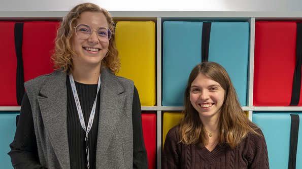 Deux jeunes femmes souriantes, devant un mur fait de rectangles colorés.