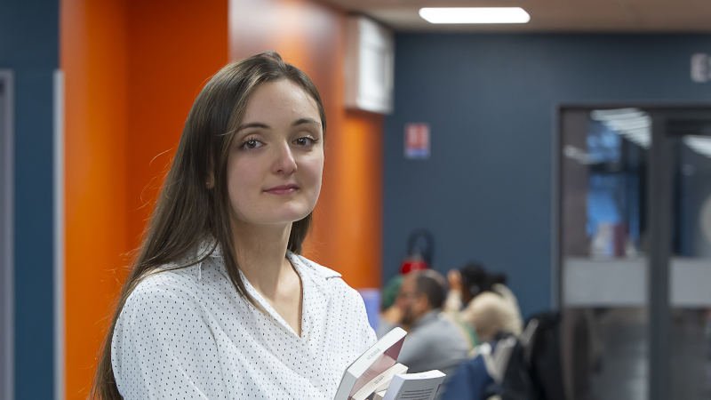 Une jeune fille, des livres à la main, dans un hall