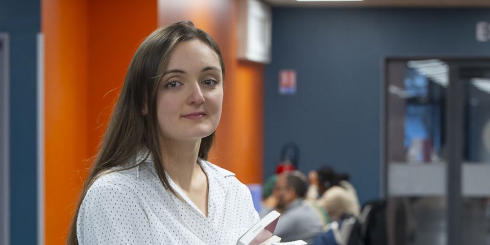 Une jeune fille, des livres à la main, dans un hall