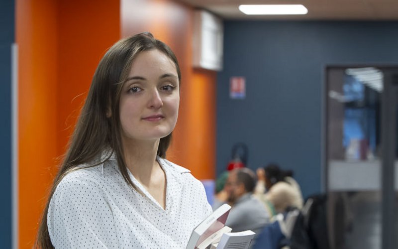 Une jeune fille, des livres à la main, dans un hall