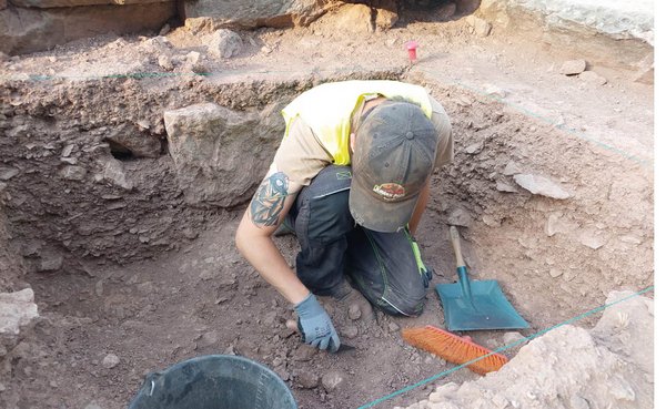 Un jeune homme, avec casquette et gants, pelle, brosse… travaille sur le sol