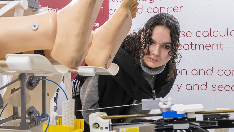 Une jeune fille, près des pieds d’un mannequin. En-dessous, on distingue une longue aiguille passant à travers une grille.