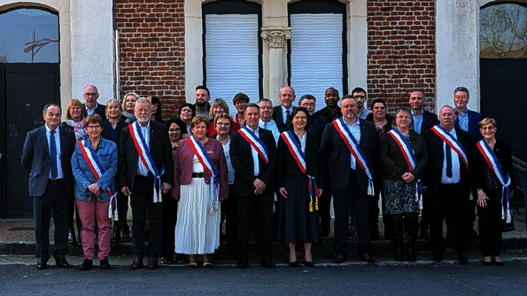 Personnes avec écharpe tricolore devant un bâtiment en briques.