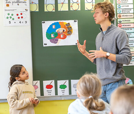 Un jeune homme, au tableau, parle à une petite fille