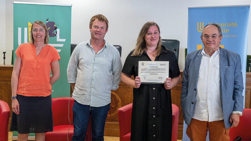 Deux hommes et deux femmes, dont une tient une affichette de prix. Derrière eux, des kakémonos