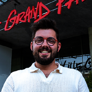 Jeune homme barbu avec lunettes, devant l’entrée d’un grand bâtiment où est écrit Lille Grand Palais