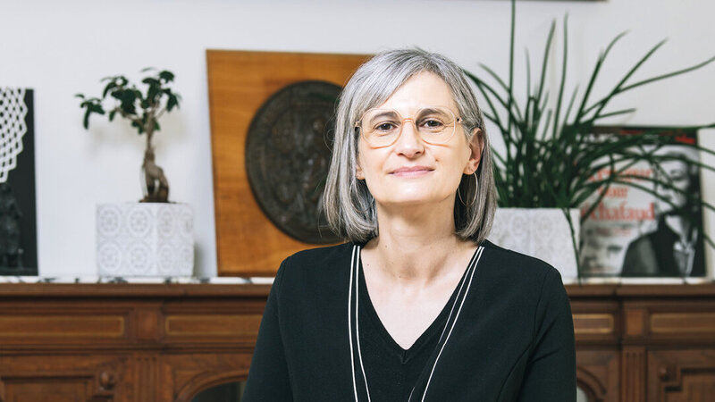 Une femme devant une sorte de buffet, à demi-assise sur un bureau, regarde l’objectif.
