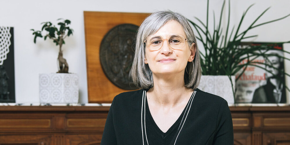 Une femme devant une sorte de buffet, à demi-assise sur un bureau, regarde l’objectif.