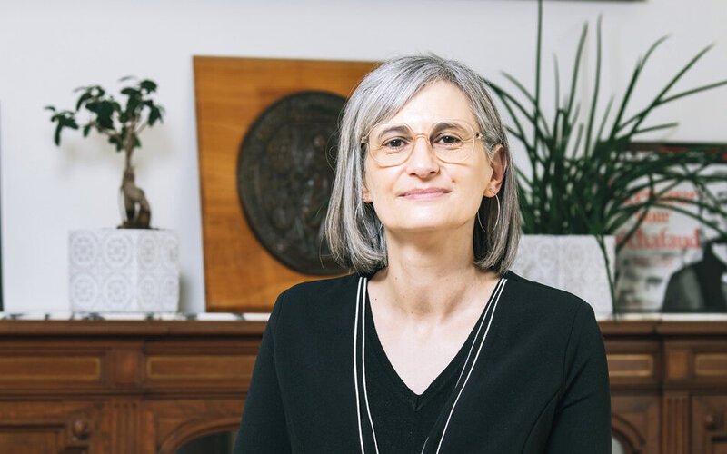 Une femme devant une sorte de buffet, à demi-assise sur un bureau, regarde l’objectif.
