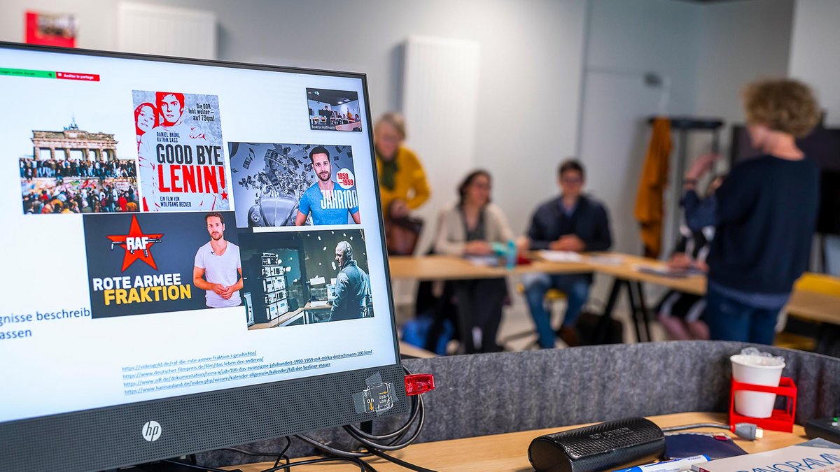 Un écran avec plusieurs images dont l’affiche du film Goodbye Lenin, et dans le fond les participants au cours, assis, et l’enseignante, debout