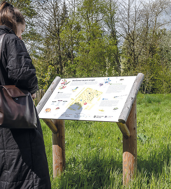 Jeune femme devant un panneau explicatif, devant une prarie et des arbustes