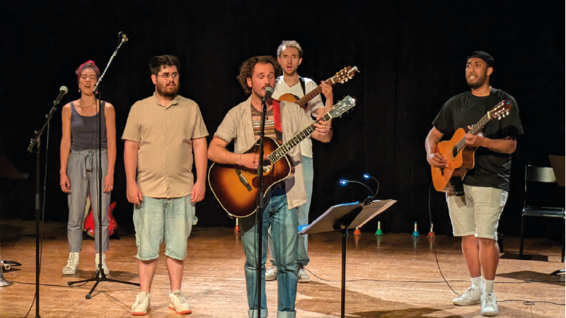 Cinq personnages debout, certains munis de guitare