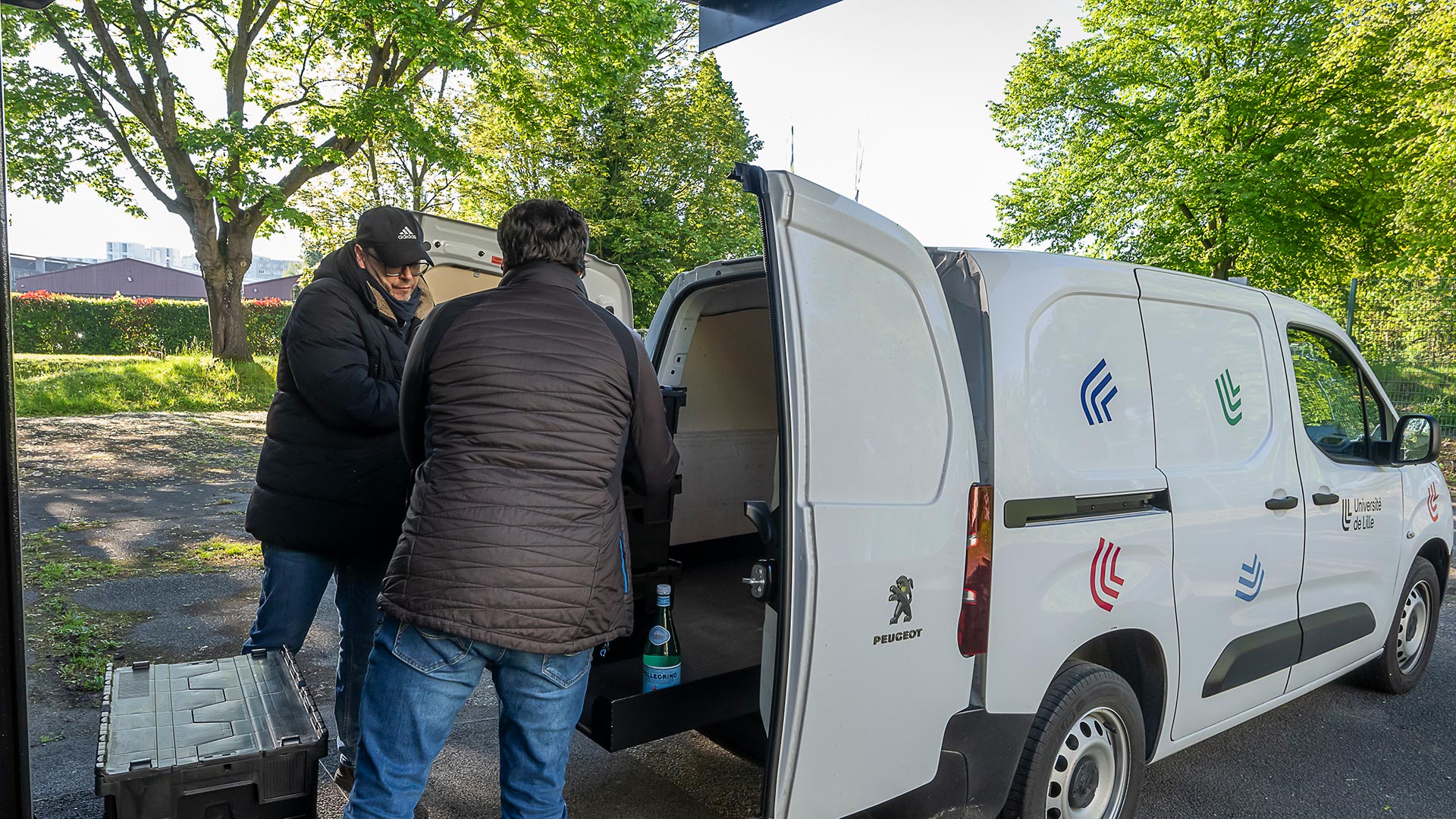 Deux hommes chargent une camionnette aux couleurs de l’université avec des caisses noires